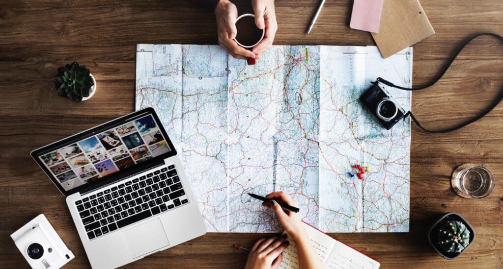 Travel planning with a map, notebook, laptop, and camera.